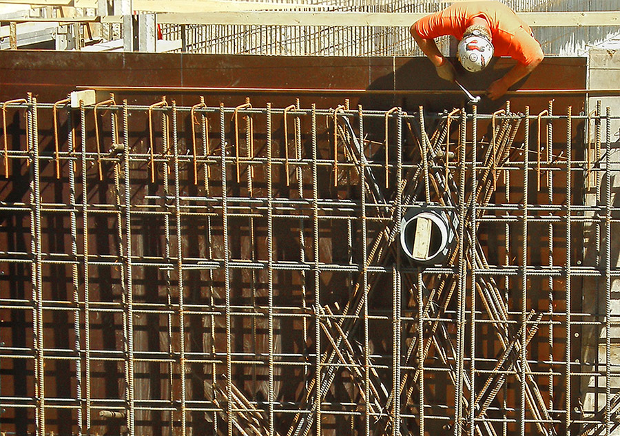 A worker laboring above a large rebar cage on a job site.