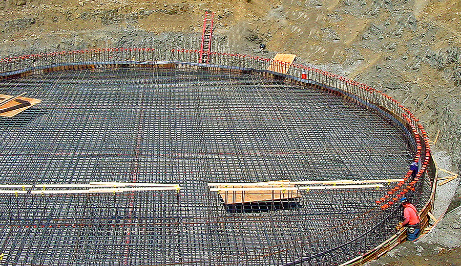 A large, round foundational rebar cage sits awaiting concrete.