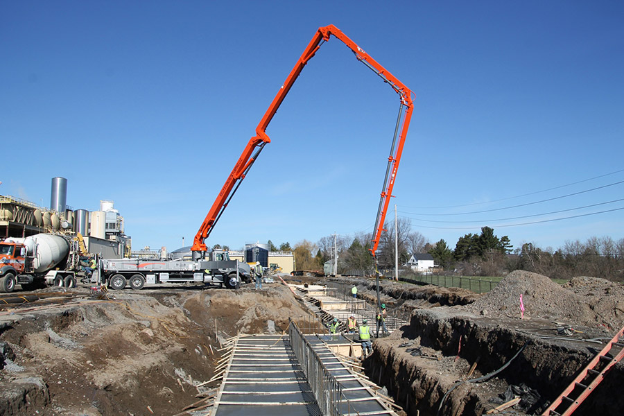 A concrete delivery crane pours concrete into a large rebar reinforced pad.