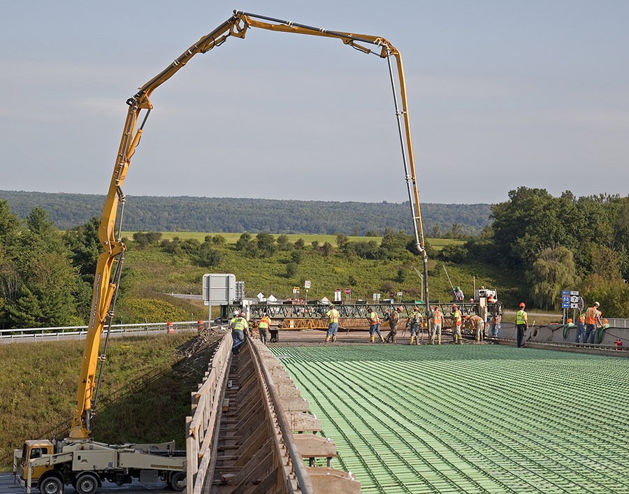 A concrete delivery crane pours concrete onto a rebar assembly during bridge resurfacing.