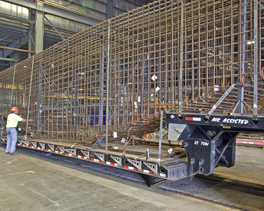 A fabricated bridge cap rebar cage is loaded onto a truck for transport.
