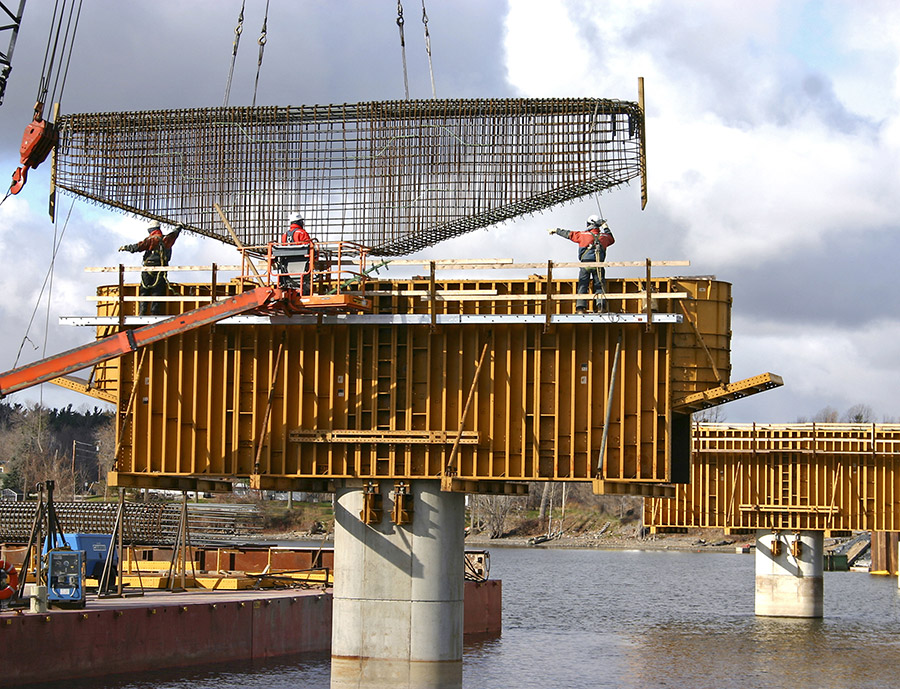 A Rebar cage is lowered by crane into a bridge pier concrete mold.